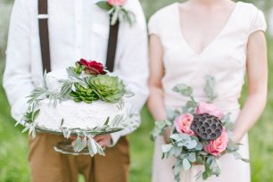 Торт, украшенный суккулентами в руках жениха и букет с коробочками лотоса в руках невесты
