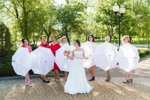 Веселые подружки невесты с белыми зонтиками позируют для фотографа