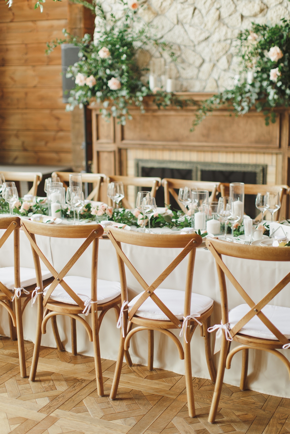 Утонченная сервировка гостевого стола, декорированного посередине гирляндой из зелени, цветов и свечей. Камин украшен свечами и композициями, деревянные стулья cross back