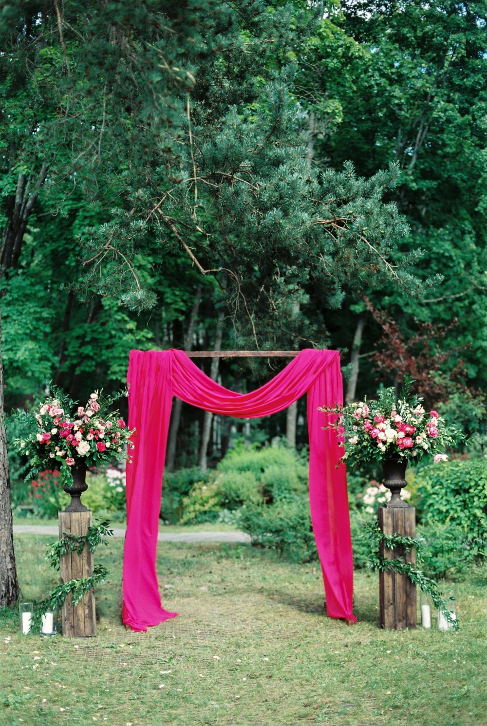 Яркую свадебную арку с драпировками легкой тканью элегантно подчеркнули пышные цветочные композиии в классических вазонах на деревянных подставках