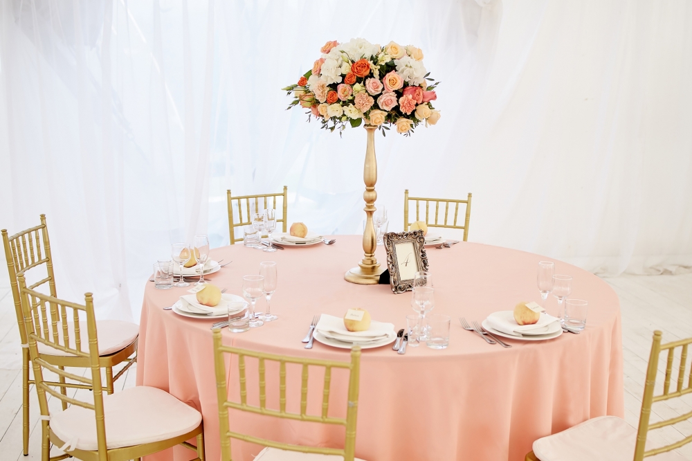Оформление столов гостей на свадьбе Александра и Кристины. Скатерти персикового цвета, пышные цветочные композиции на высоких золотистых подставках, золотистые стулья кьявари и, конечно, персики