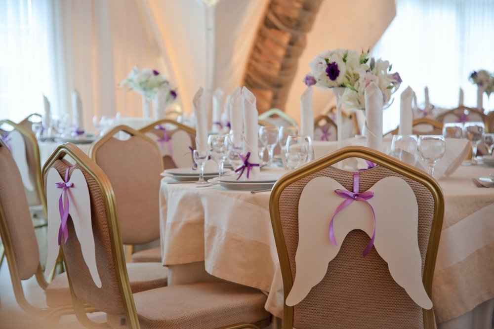 Оформление зала. На стульях "ангельские" крылья из перламутровой бумаги, декорированные атласным бантом и стразинкой.