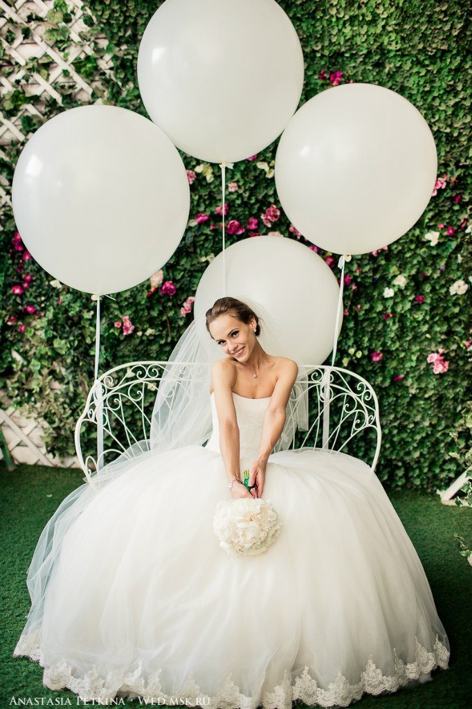 Фотосессия невесты на фоне цветочной фотозоны с большими белыми шарами