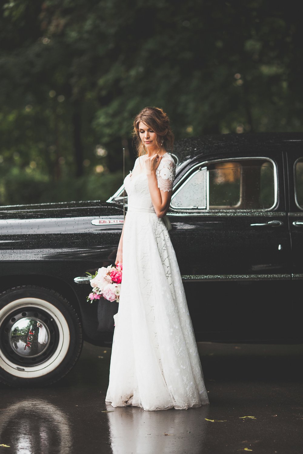 Невеста в кружевном платье с рукавами у свадебного ретро автомобиля