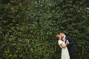 Поцелуй молодоженов на фоне зеленой стены