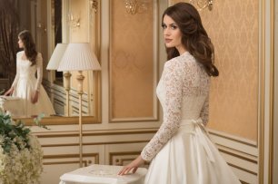 Модель Диас. Платье А-силуэта из шелкового микадо, поверх декольтированного платья с прямым срезом корсета одевается жакет из кордового кружева. Юбка в бантовую складку сзади переходит в шлейф средней длины, в боковых швах спрятаны кармашки. Волшебная мод