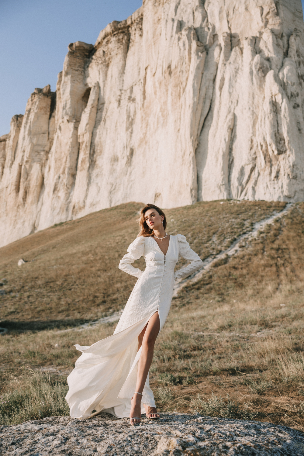 Легкое свадебное платье из жатой воздушной тафты с рукавами буфф, высоким разрезом на юбке и пуговицами из натурального жемчуга.