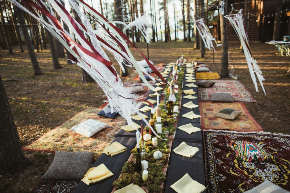 Стол для гостей на свадьбе в стиле хиппи-фестиваля Woodstock. Ковры и подушки, столы из поддонов, мох, перья и разномастные бутылочки