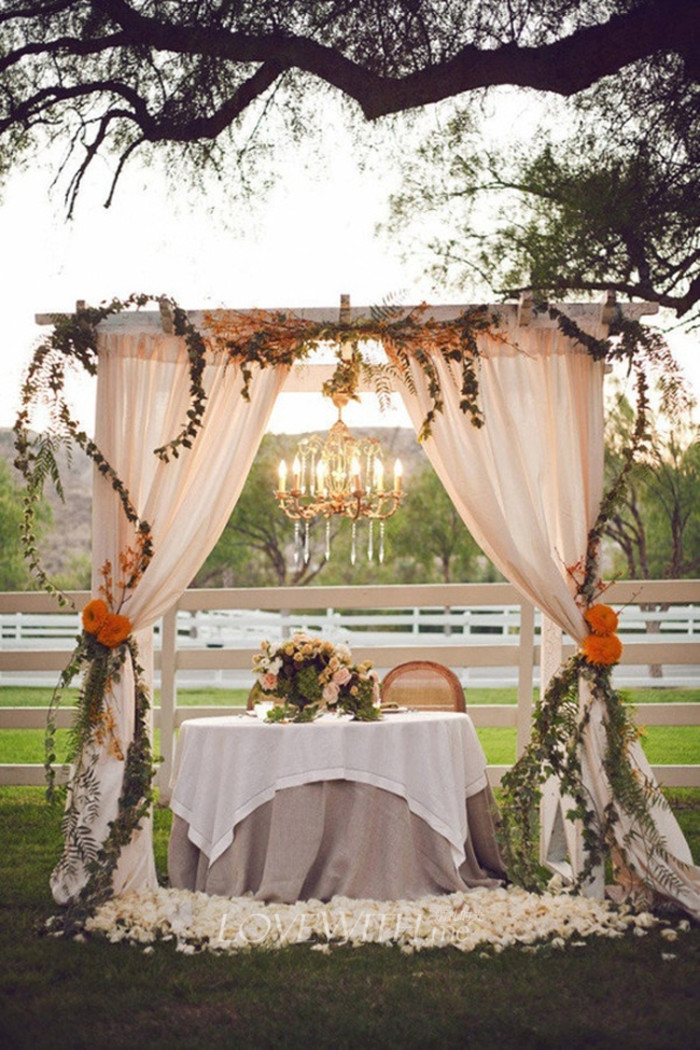 Свадебная арка, украшенная цветами и плотной струящейся тканью