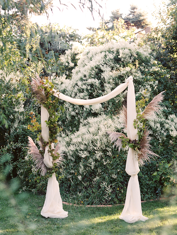 Свадебная арка, украшенная плотной тканью, перьями и растительностью