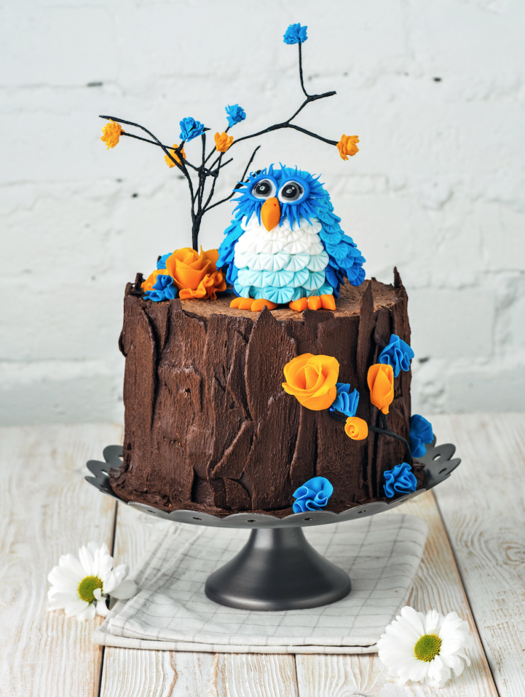 Детский торт-пенёк ,имитация которого создана из натурального тёмного шоколада. Украшает пенёк фигурка совы и маленькие бутончики роз из сахарной пасты.