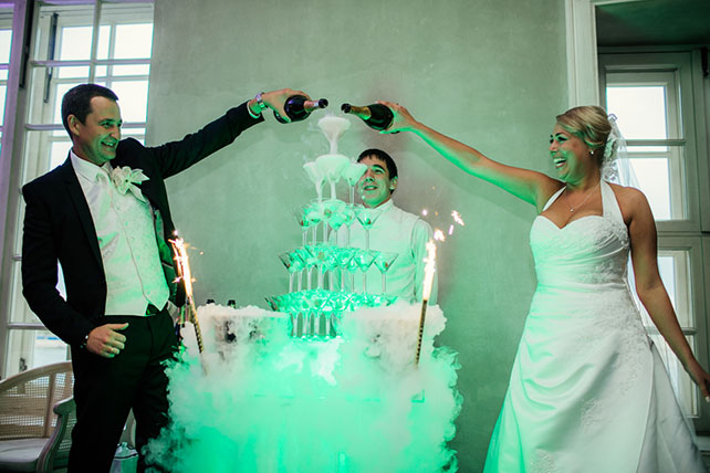 Свадьба в английском стиле, молодожены наливают шампанское в бокалы в пирамиде