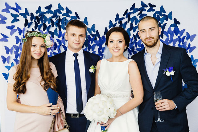 Элегантная черничная свадьба, молодожёны с друзьями на фоне фотозоны