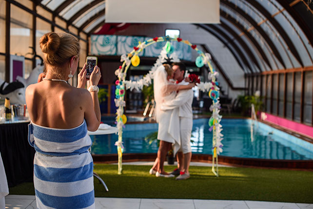 Весёлая свадьба у бассейна, подружка фотографирует на телефон поцелуй жениха и невесты